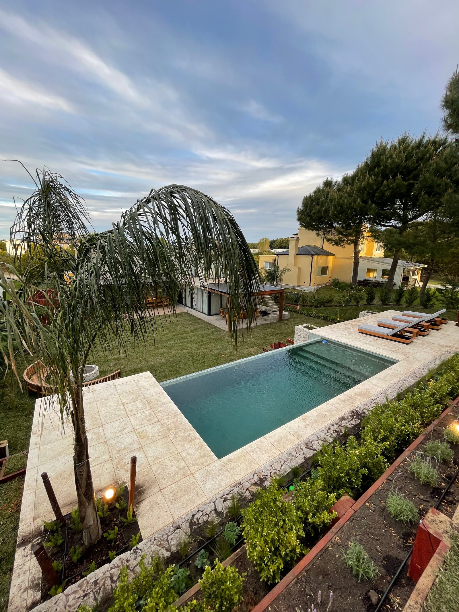 Piscina infinita moderna con deck de piedra y vegetación exuberante — proyecto COSTA ESMERALDA, por Baires Green, en Pinamar