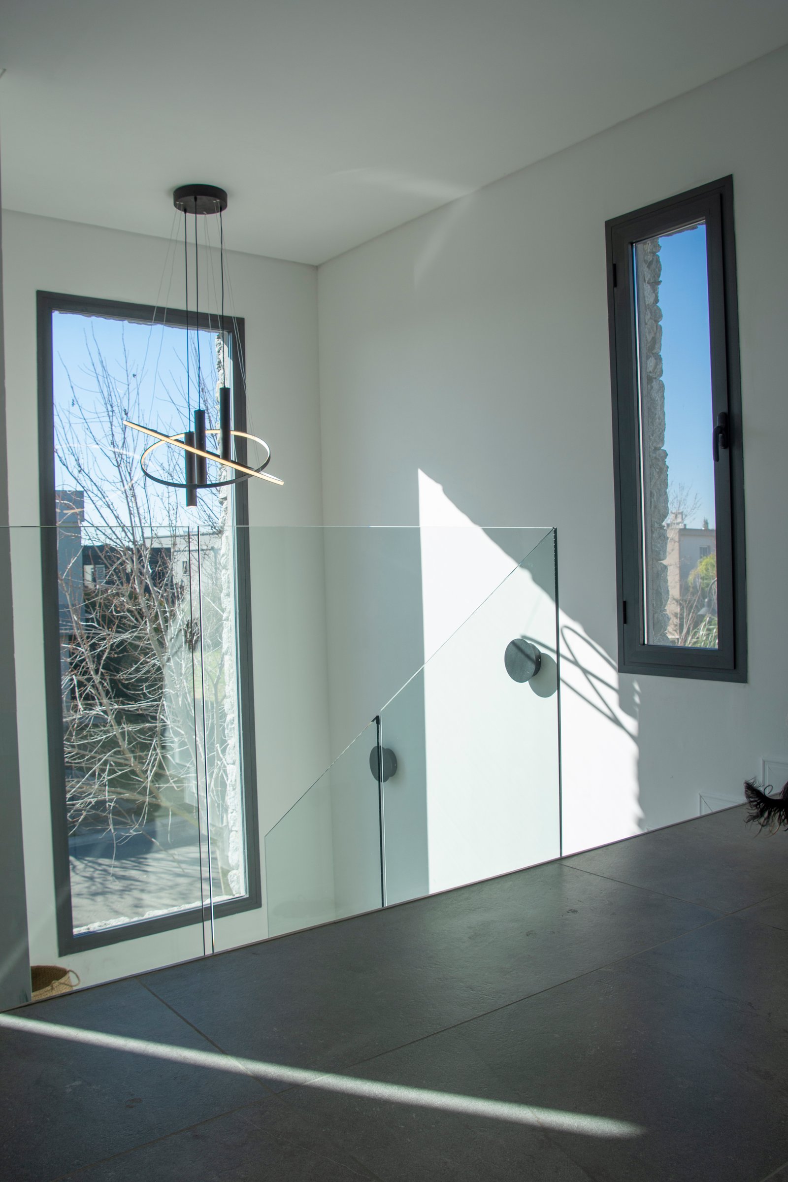 Escalera moderna con barandas de vidrio y luz colgante — proyecto Casa Tipas, por MSMC, en Сармьенто 3830