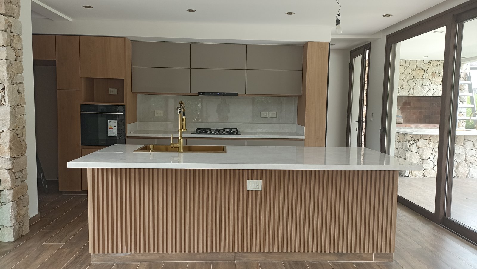 Cocina moderna con isla de madera acanalada y mesada de piedra blanca — proyecto Vivienda en Fincas de Hudson, por Monarq Arquitectura, en C. 137 7400