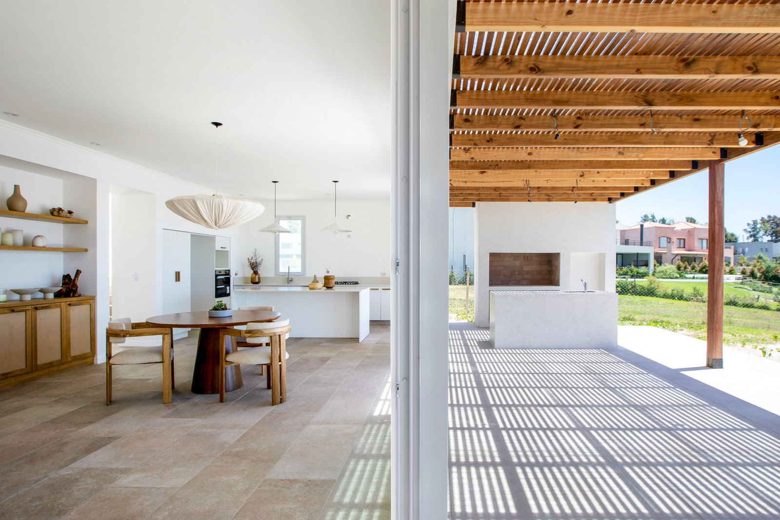 Sala de jantar e cozinha moderna integrada, com pérgola de madeira e piso de pedra — projeto OBRA LE PIETRE DEL CASALE SABBIA, por ILVA, em Provincia de Buenos Aires