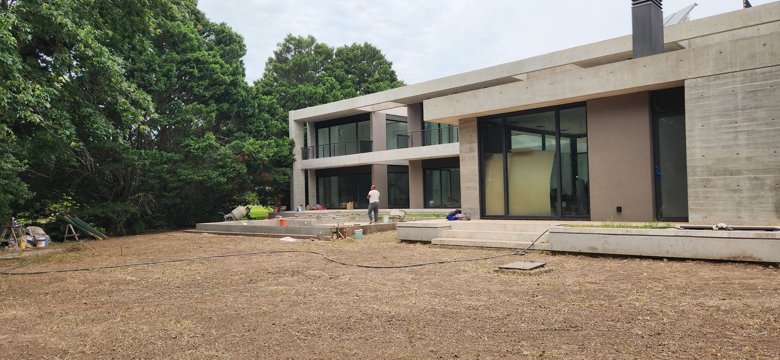 fachada moderna de hormigón en construcción con vegetación — proyecto Casa CAD, por Estudio Rifahi, en Moreno