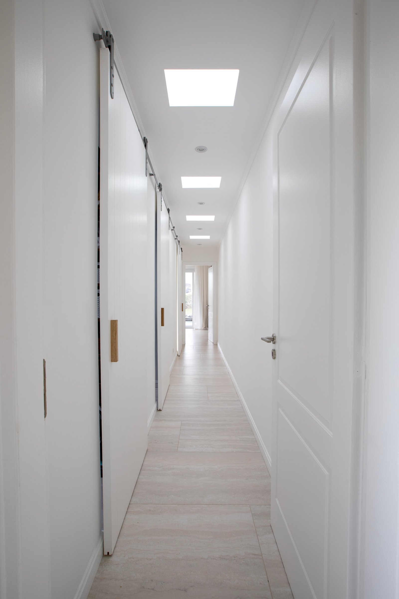 Pasillo moderno y luminoso con puertas corredizas y tragaluces — proyecto OBRA EL RETIRO, por ILVA, en Provincia de Buenos Aires