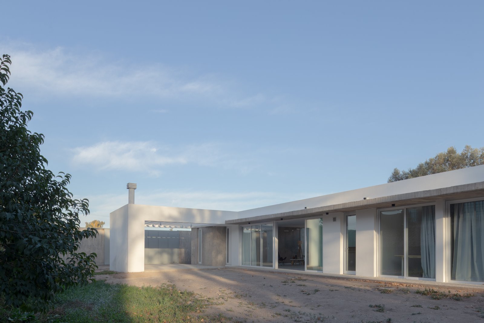 Casa moderna de concreto branco com grandes janelas e pátio — projeto Vivienda CCE, por ONA - Oficina Nómada de Arquitectura, em M5505 Chacras de Coria