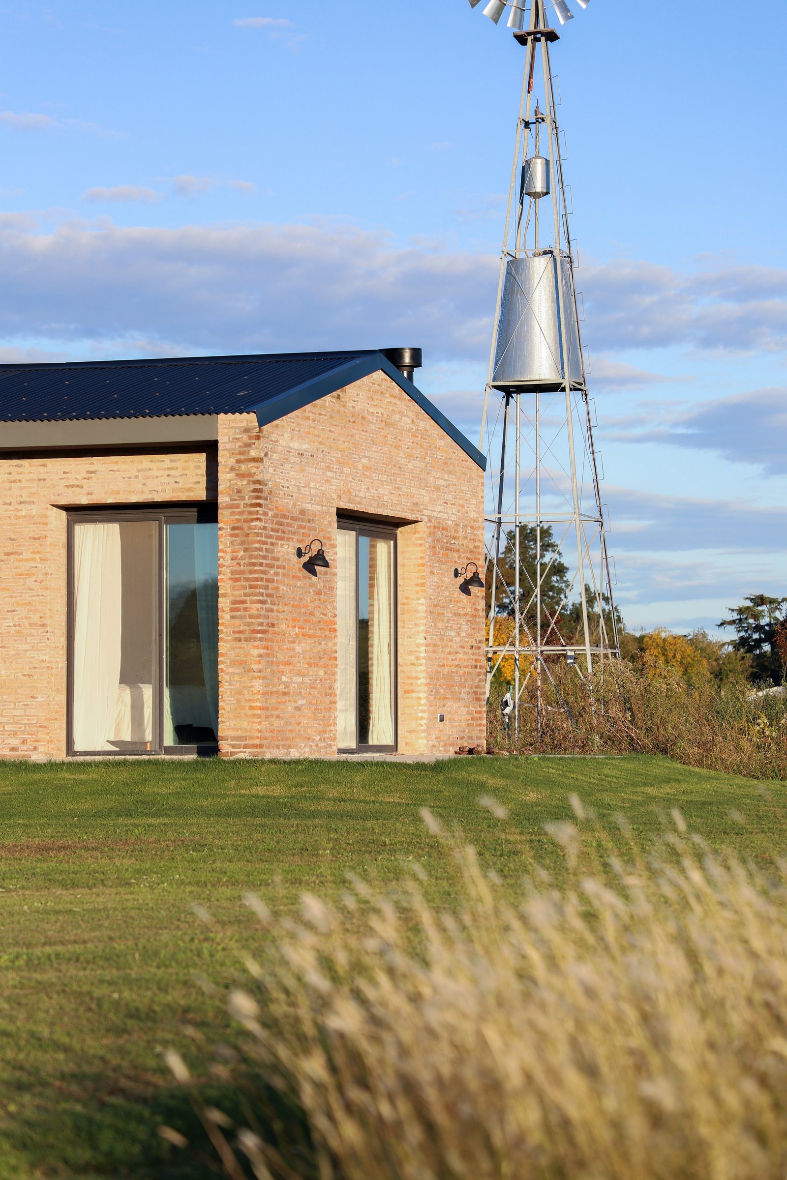 Casa moderna de ladrillo visto con molino de viento antiguo en el campo — proyecto Casa Areco, por R+B arquitectos, en San Antonio de Areco