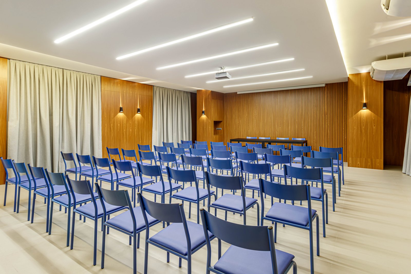 Sala de conferencias con sillas azules y paneles de madera — proyecto Auditorio Inforcell, por Ricardo Mota, en Manaus