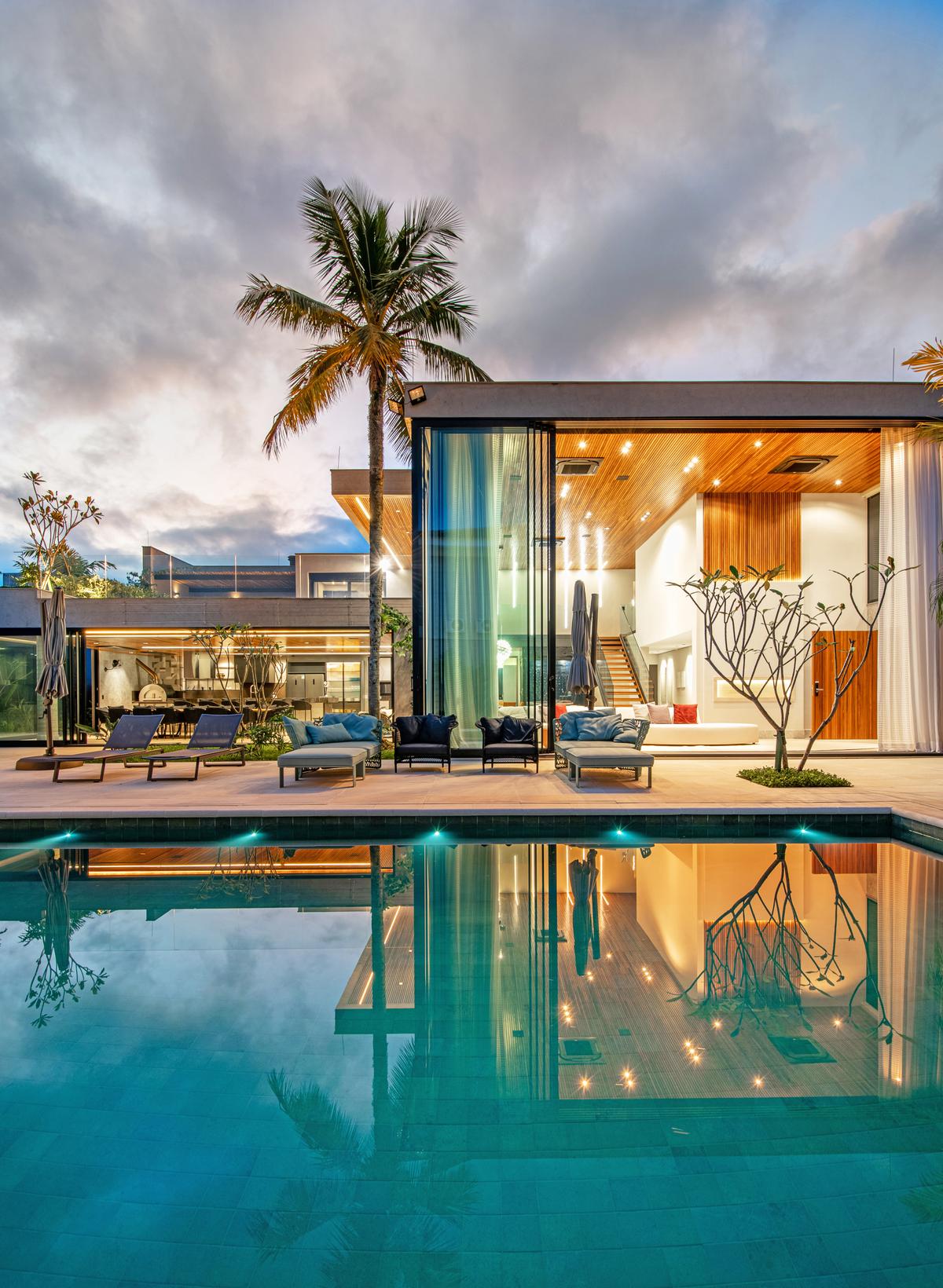 Casa moderna com piscina iluminada e palmeiras ao entardecer — projeto Sombra E Agua Fresca, por Carlos Pardal