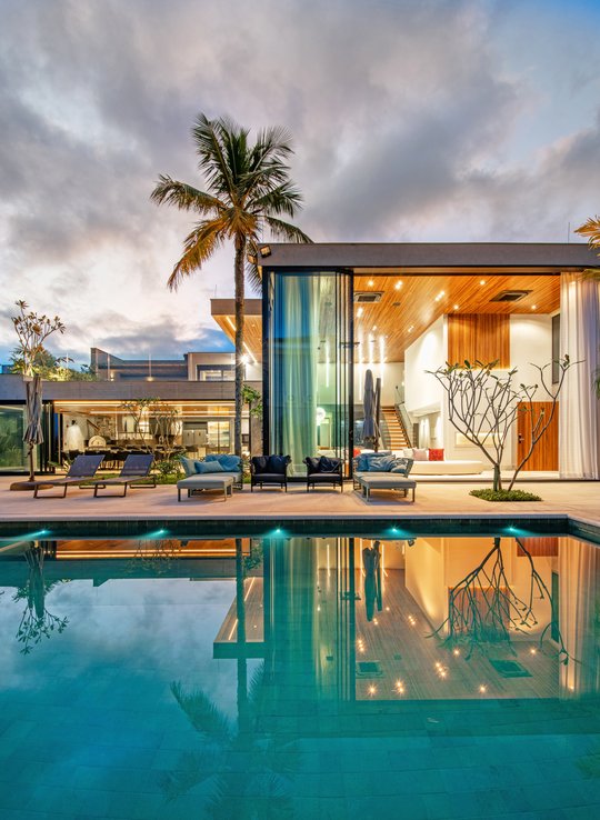 Casa moderna con piscina iluminada y palmeras al atardecer — proyecto Sombra E Agua Fresca, por Carlos Pardal