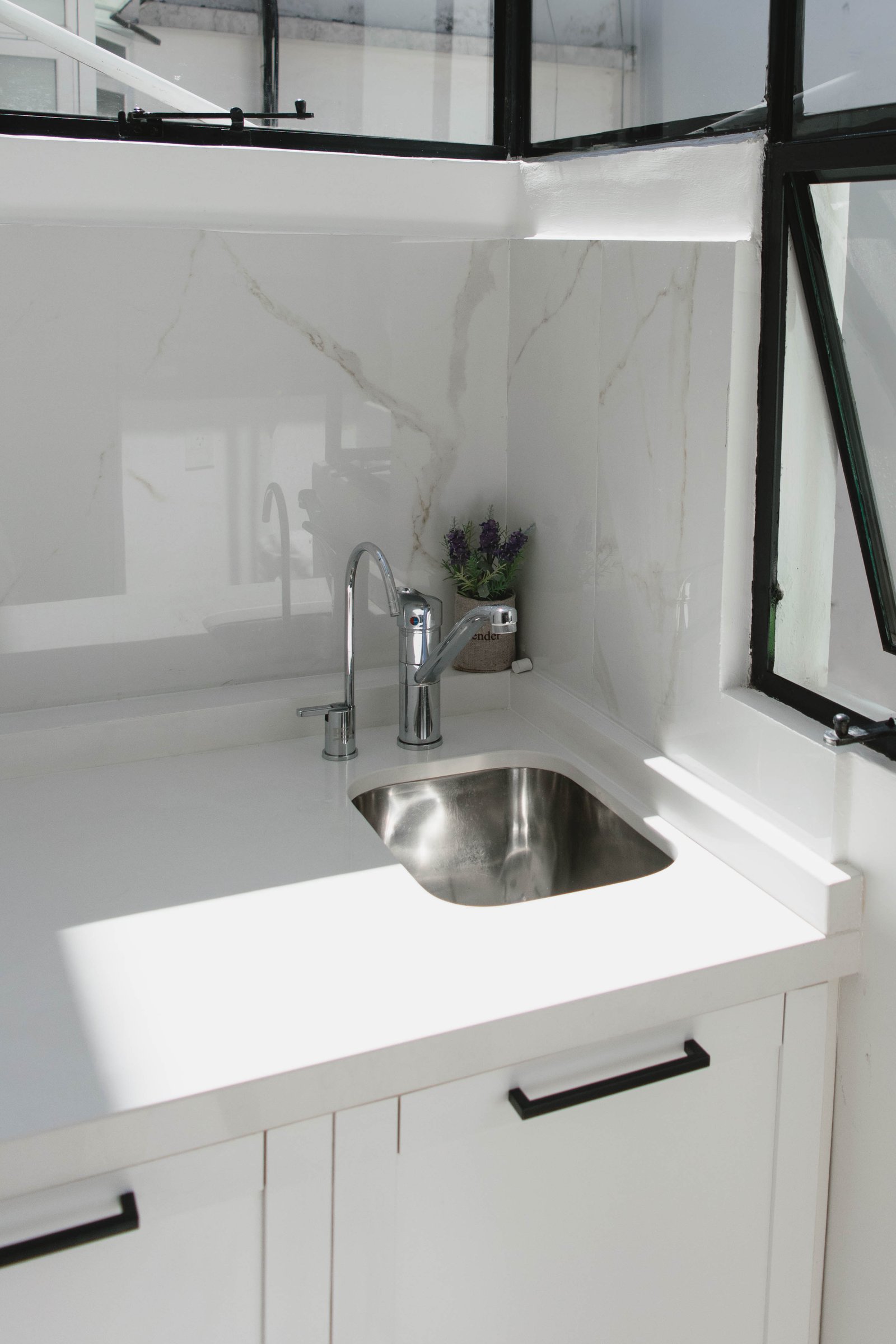 Cozinha moderna com bancada branca, torneira cromada e parede de mármore — projeto Goyena, por Martina Kleinert, em Caballito