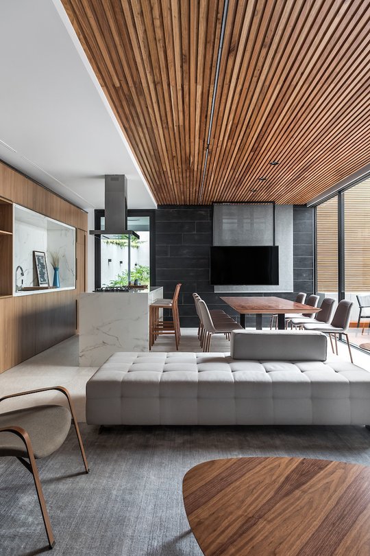 Living comedor con cocina integrada, techo de listones de madera y pared de piedra negra — proyecto Bidese Gourmet, por Boscardin Corsi Arquitetura