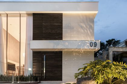 Fachada moderna de residencia con revestimiento piedra y madera oscura e iluminación cálida — proyecto Casa MC, por Boscardin Corsi Arquitetura