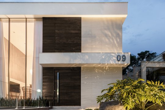 Fachada moderna de residencia con revestimiento piedra y madera oscura e iluminación cálida — proyecto Casa MC, por Boscardin Corsi Arquitetura
