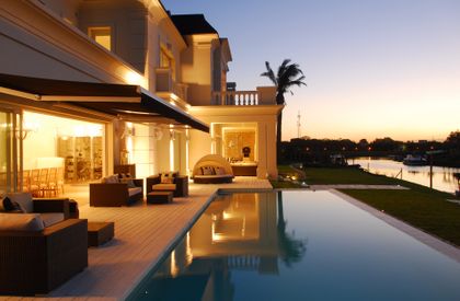 Pileta infinita moderna con mobiliario exterior y luces cálidas al atardecer — proyecto Chateau al Río, por Apaarquitectura, en Tigre