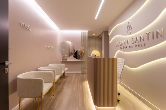 Interior comercial moderno beige con paredes curvas e iluminación indirecta, recepción de madera y sillas de espera — proyecto #ConsultórioSusanaSantin, por Oficina de Morar