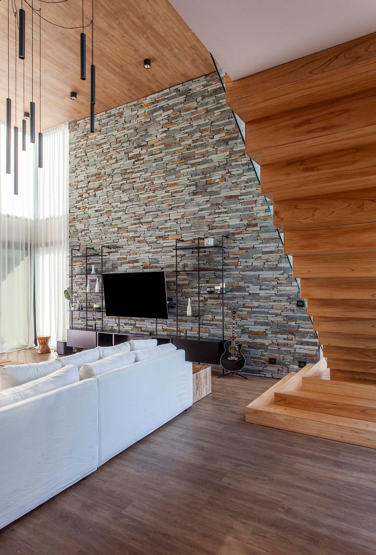 Living moderno con pared de piedra, escalera de madera y sofá blanco — proyecto CASA T199, por A'PRIMA - Arquitectura Sustentable, en Los Robles 5901