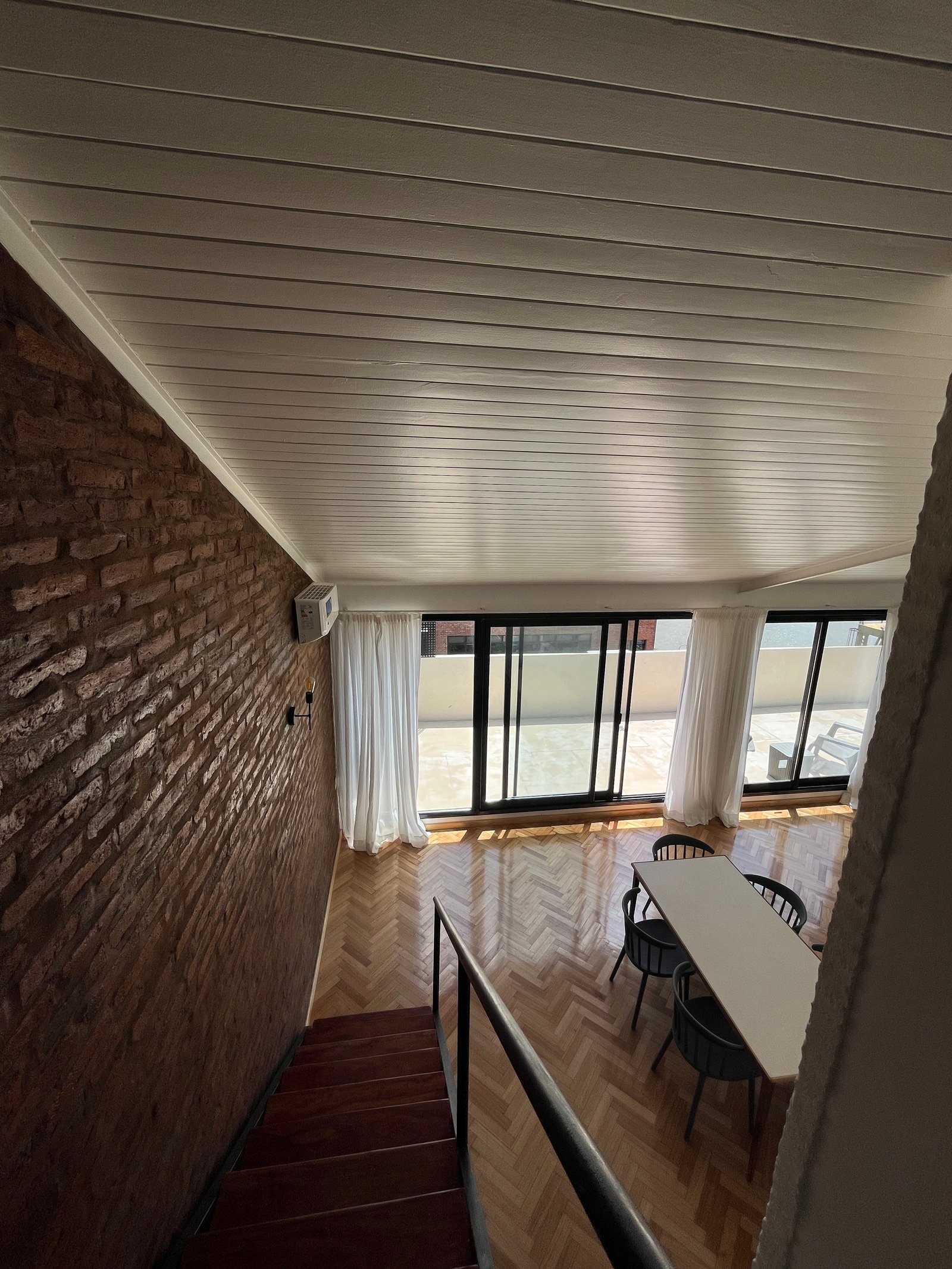 Sala moderna com parede de tijolos expostos e grandes janelas — projeto Departamento Puerto Madero, por Arcucci Arquitectura, em Puerto Madero