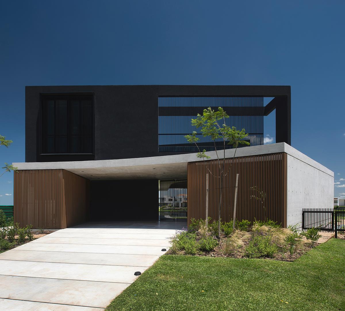 Fachada moderna de dois andares com volumes geométricos e detalhes em madeira — projeto CASA MUELLES, por GMARQ, em Escobar