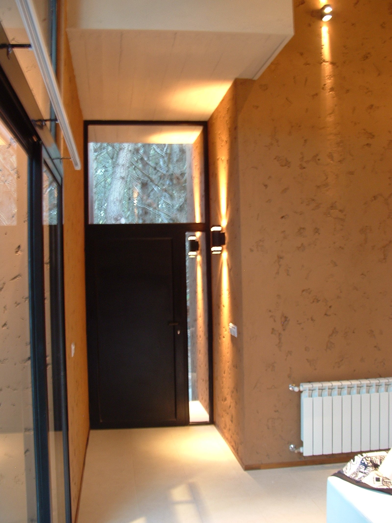 Pasillo moderno con puerta negra, ventana al bosque y pared texturizada — proyecto LA  ALHAMBRA, por GJF estudio, en Costa del Este