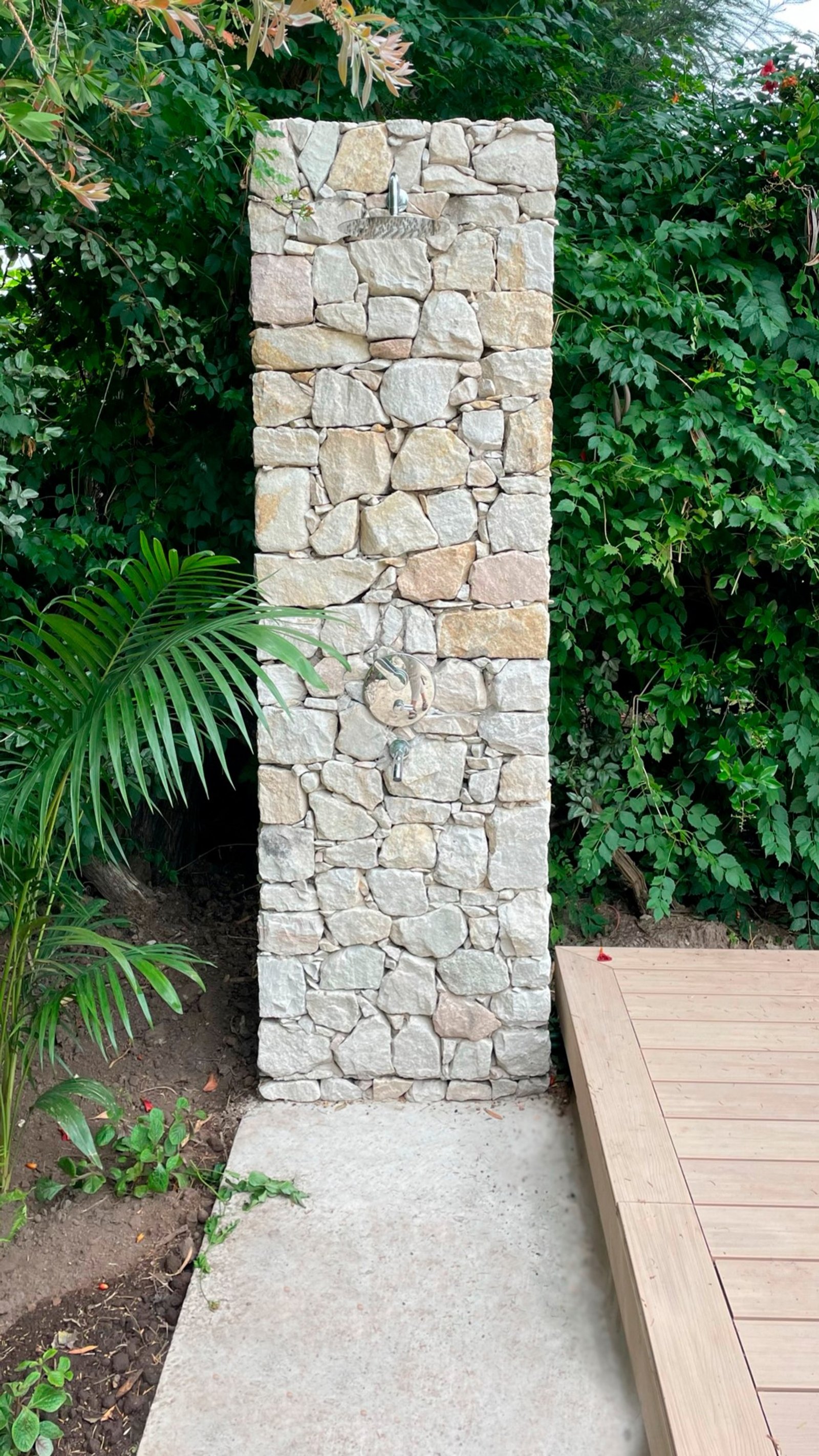 Ducha externa de pedra com deck de madeira e vegetação exuberante — projeto Casa CC, por Hermann Arquitectos, em Los Castores
