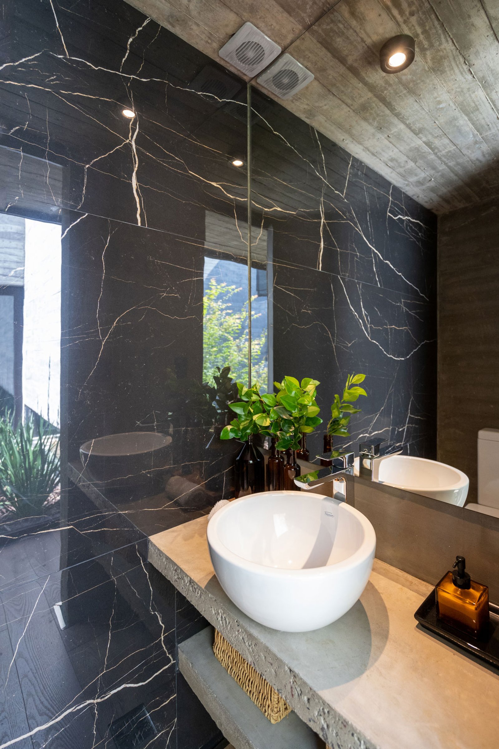 Baño moderno con paredes de mármol negro y detalles de cemento — proyecto Casa Tres Patios, por Besonías Almeida arquitectos, en Pilar