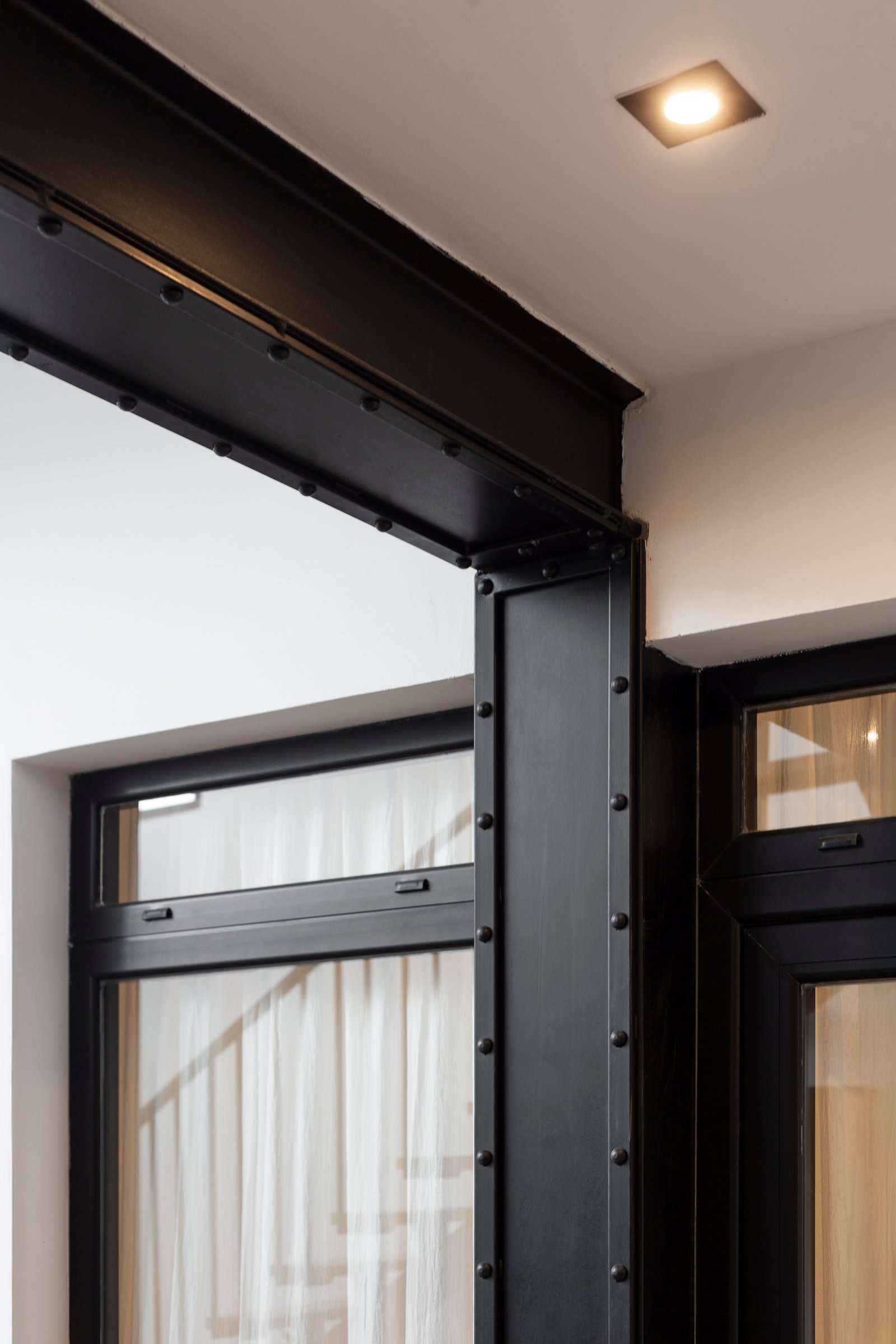 Detalhe arquitetônico industrial com vigas de aço pretas e janelas amplas — projeto JURAMENTO, por Nima Estudio, em Buenos Aires