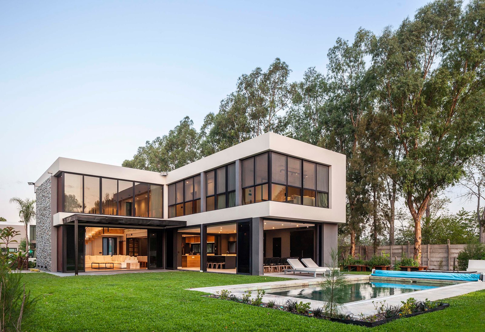 Fachada moderna con piscina infinita y jardín frondoso — proyecto CASA T199, por A'PRIMA - Arquitectura Sustentable, en Los Robles 5901