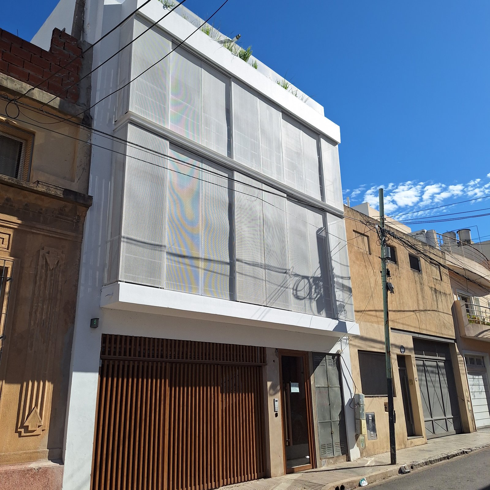 Fachada moderna com malha metálica e porta de garagem de madeira — projeto Edificio Escribano, por LW Lopez Wolder arquitectos, em Pasaje Escribano 66