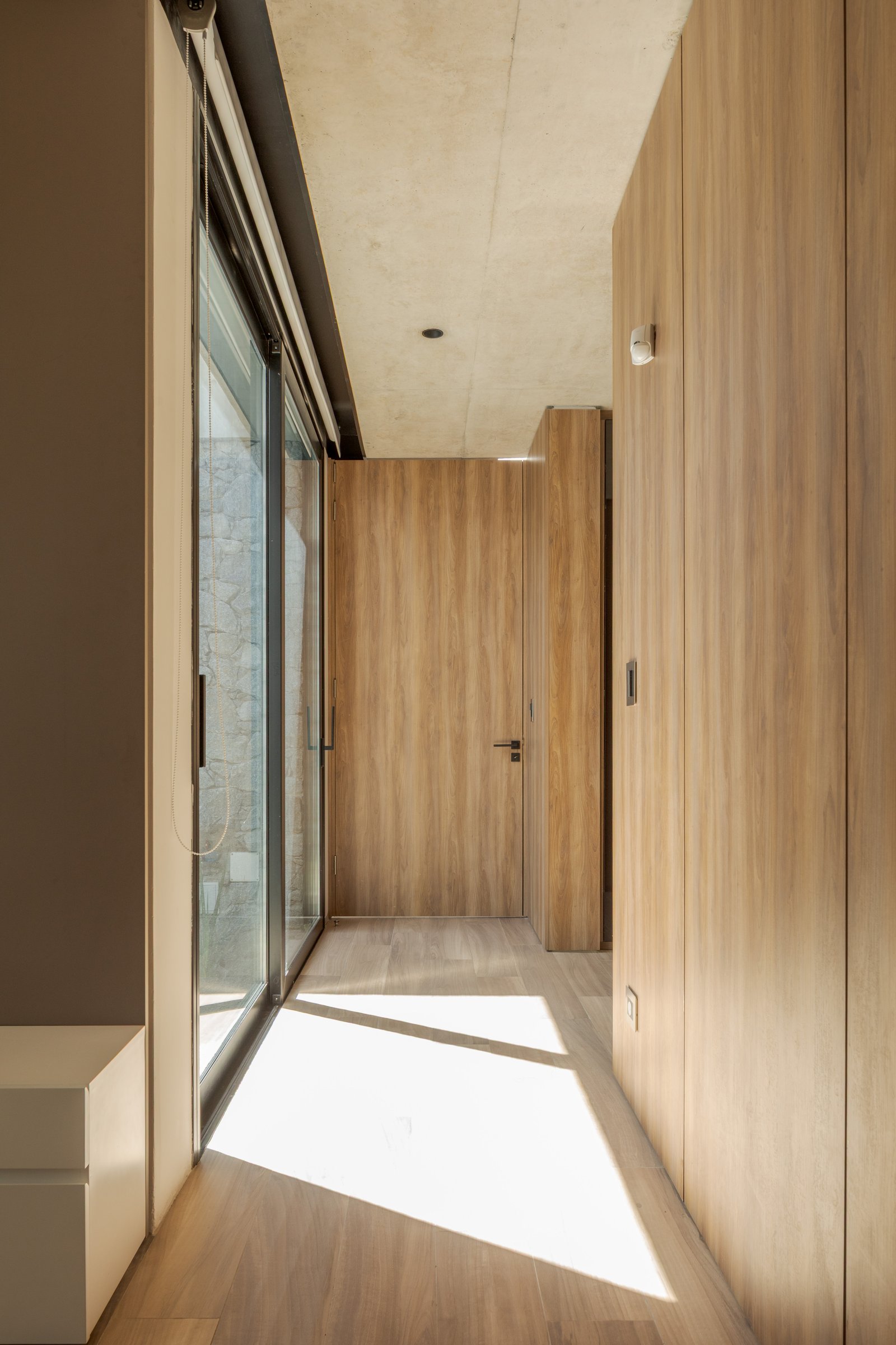 Pasillo moderno con paneles de madera y luz solar — proyecto Casa PLANALTO, por Grupo CRBN, en Av. Pres. Perón 10298