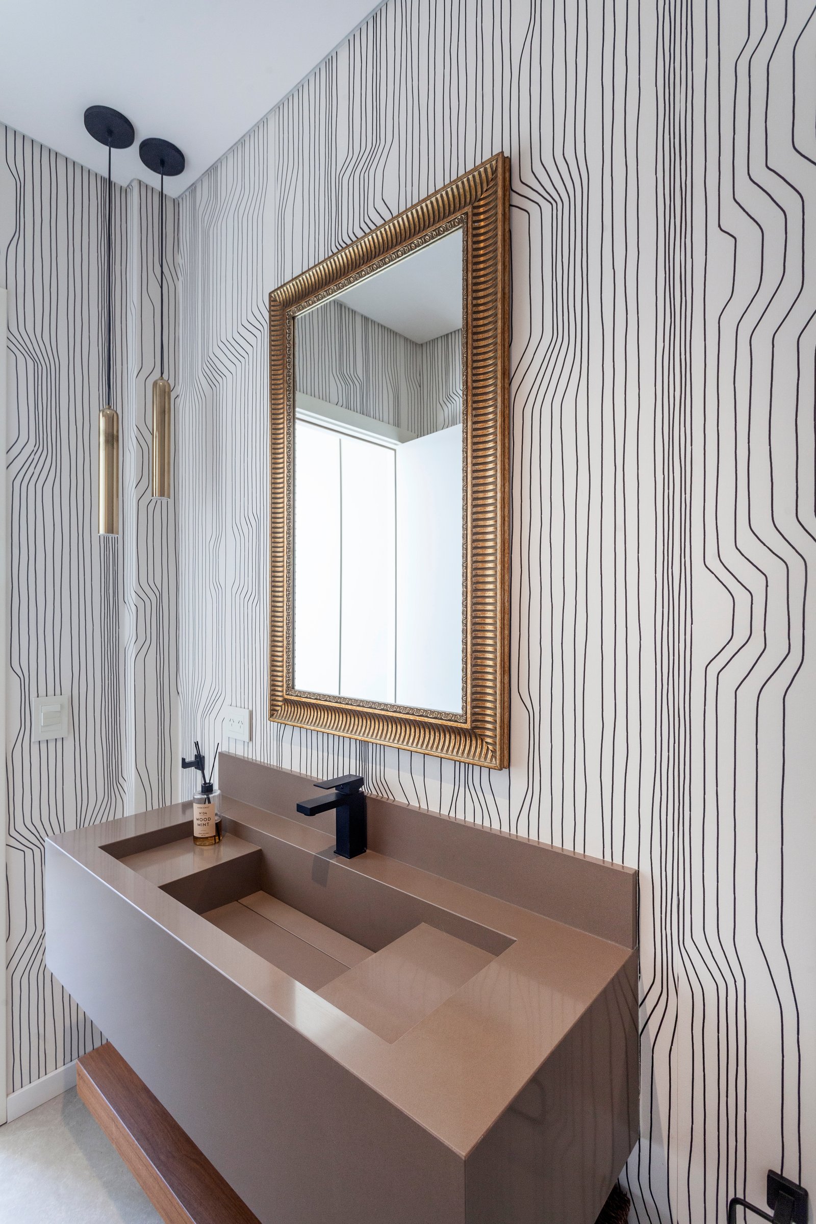 Baño moderno con papel tapiz gráfico, espejo dorado y bacha de piedra integrada — proyecto CASA M40, por A'PRIMA - Arquitectura Sustentable, en Unnamed Road