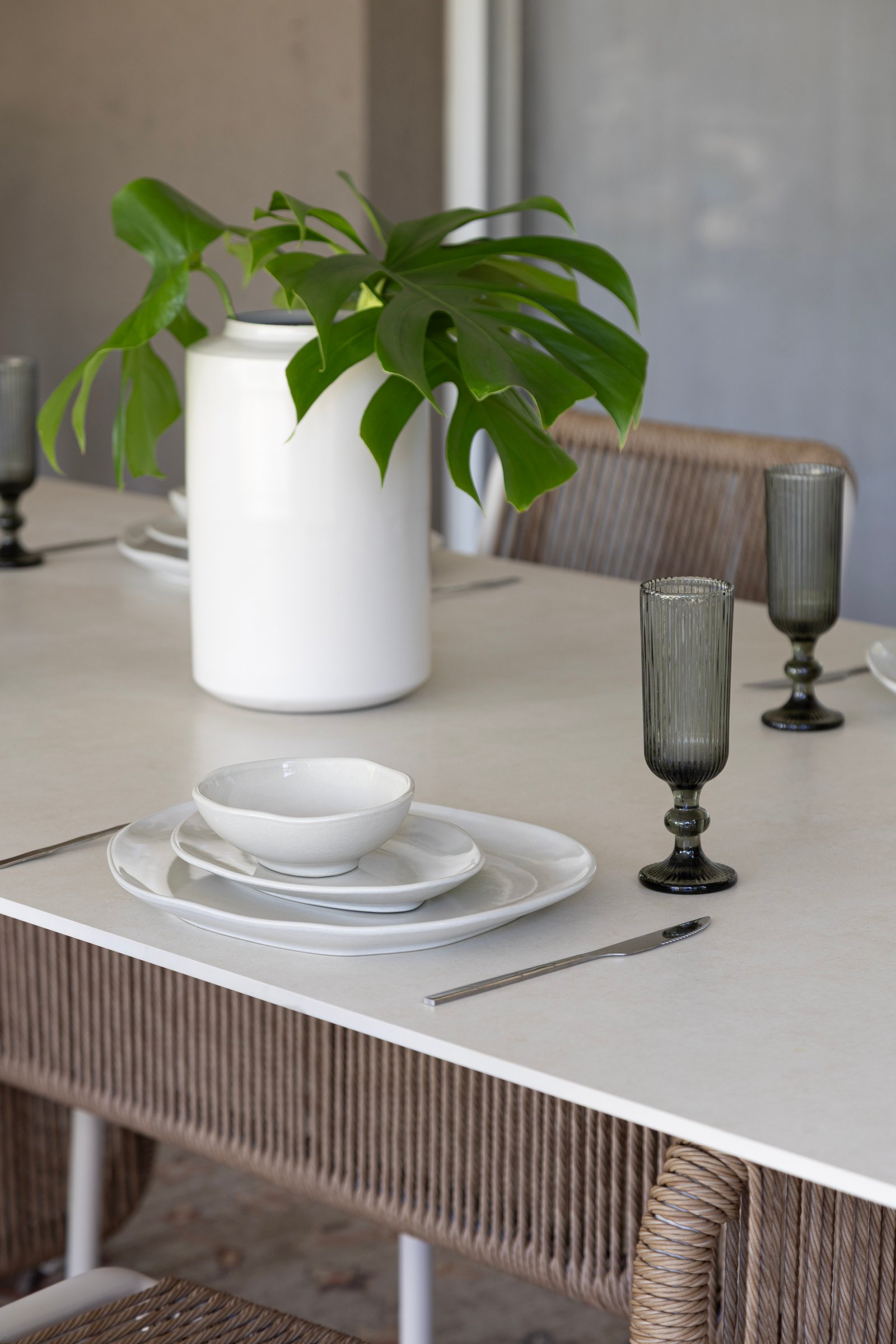 Comedor exterior con planta monstera, sillas de ratán y mesa blanca — proyecto Nuevos diseños de Muebles de Exterior , por DESDE ASIA, en Malabia 1359
