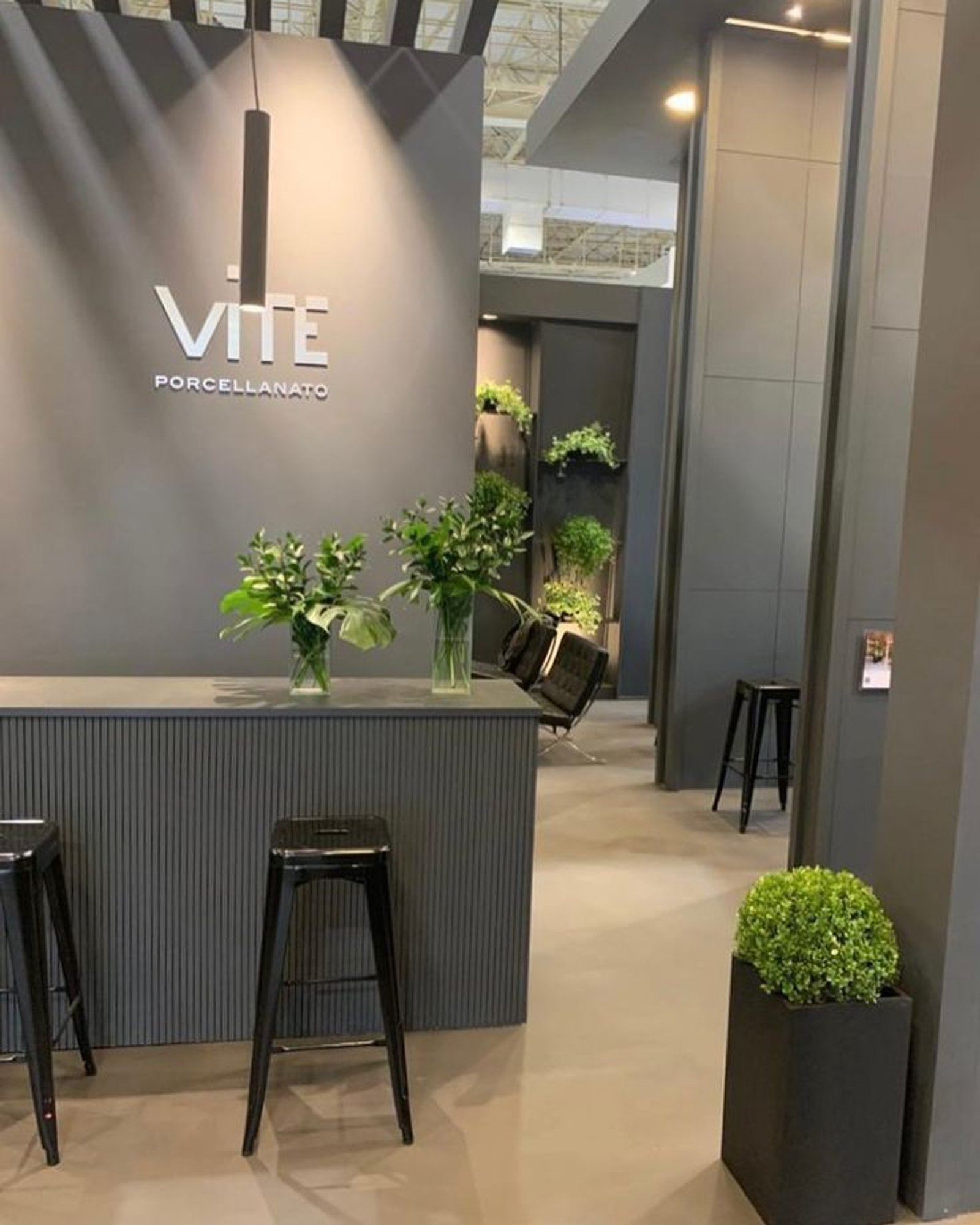 Espaço comercial moderno com logo VITE, balcão cinza e bancos pretos — projeto Expo Revestir 2022, por Vite Porcellanato, em São Paulo