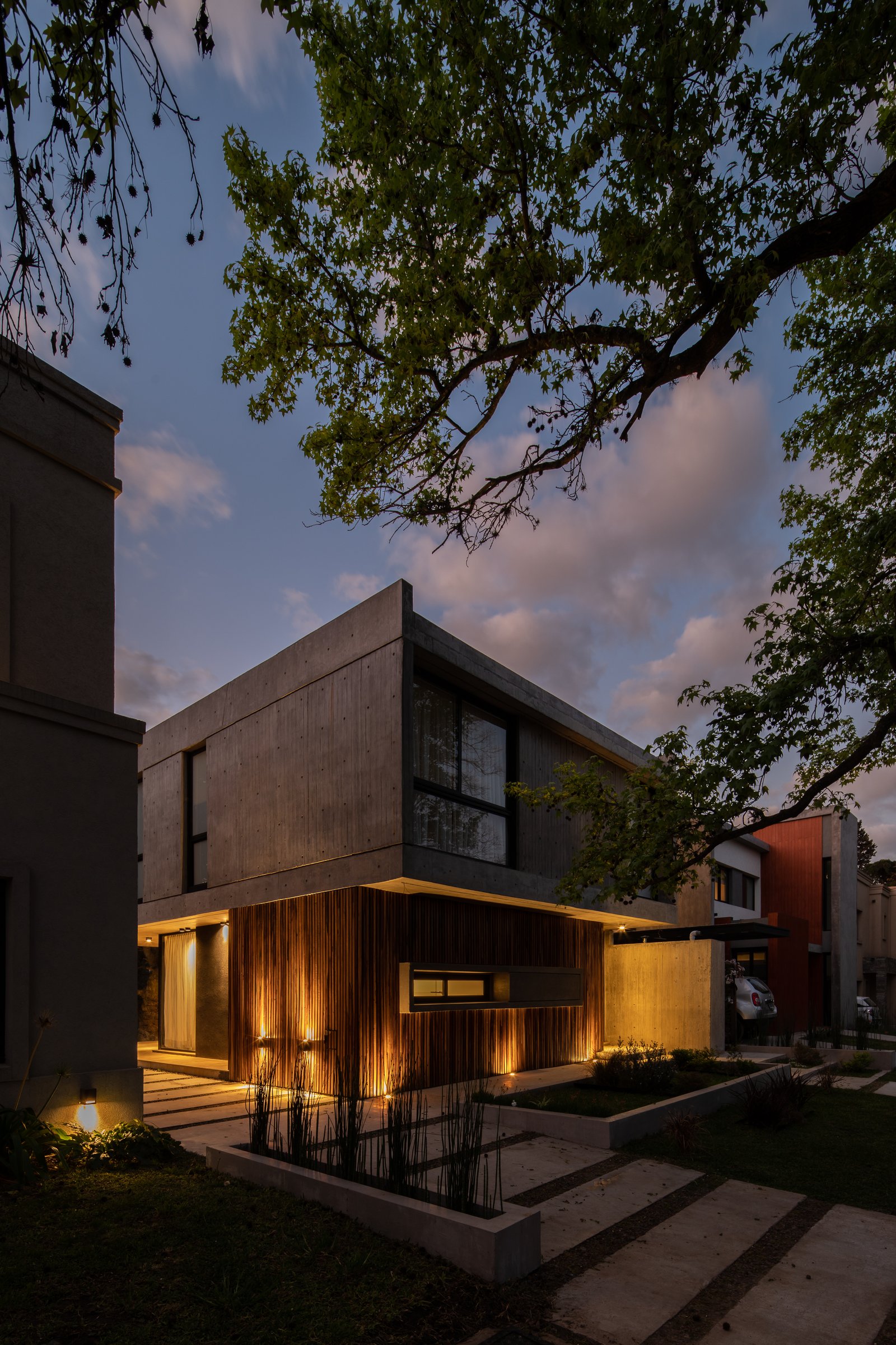 Fachada moderna con hormigón, madera y luces cálidas — proyecto Casa Emilia, por Grupo CRBN, en Parque Leloir