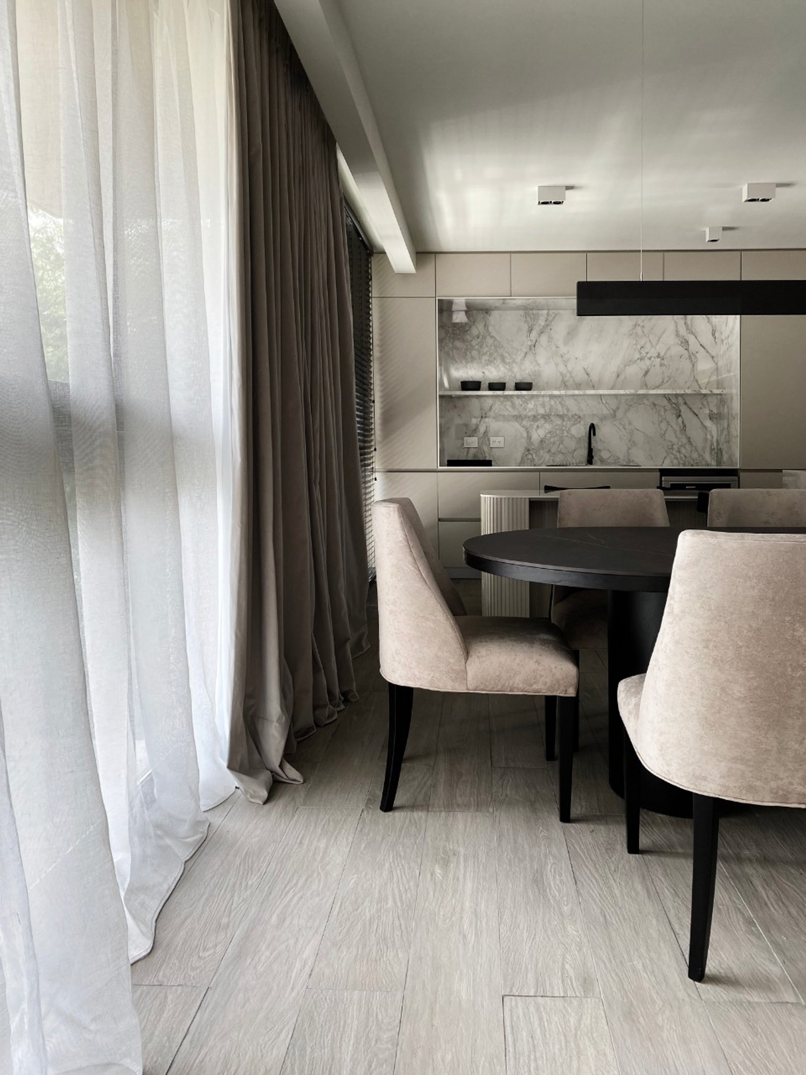 Comedor moderno con mesa redonda negra y sillas beige, cocina de mármol — proyecto Pampa, por ABEJA CONCEPT, en Belgrano