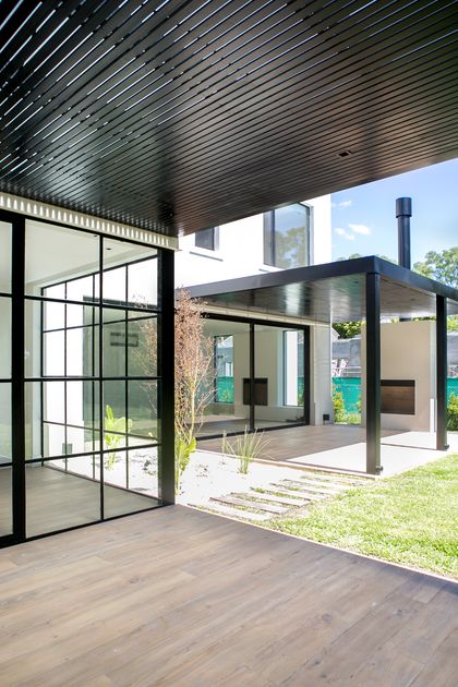 Patio moderno con pérgola de metal negro y ventanales de piso a techo — proyecto Bosque Chico, por Estudio Arq. María Sioli, en Garin
