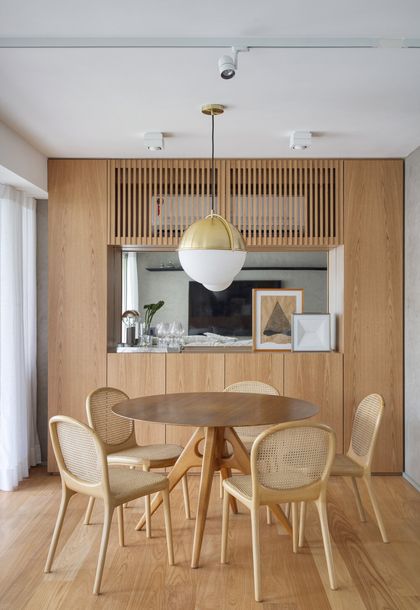 Comedor moderno con mesa redonda y sillas de ratán bajo lámpara dorada — proyecto JG House, por Studio Ro-ca