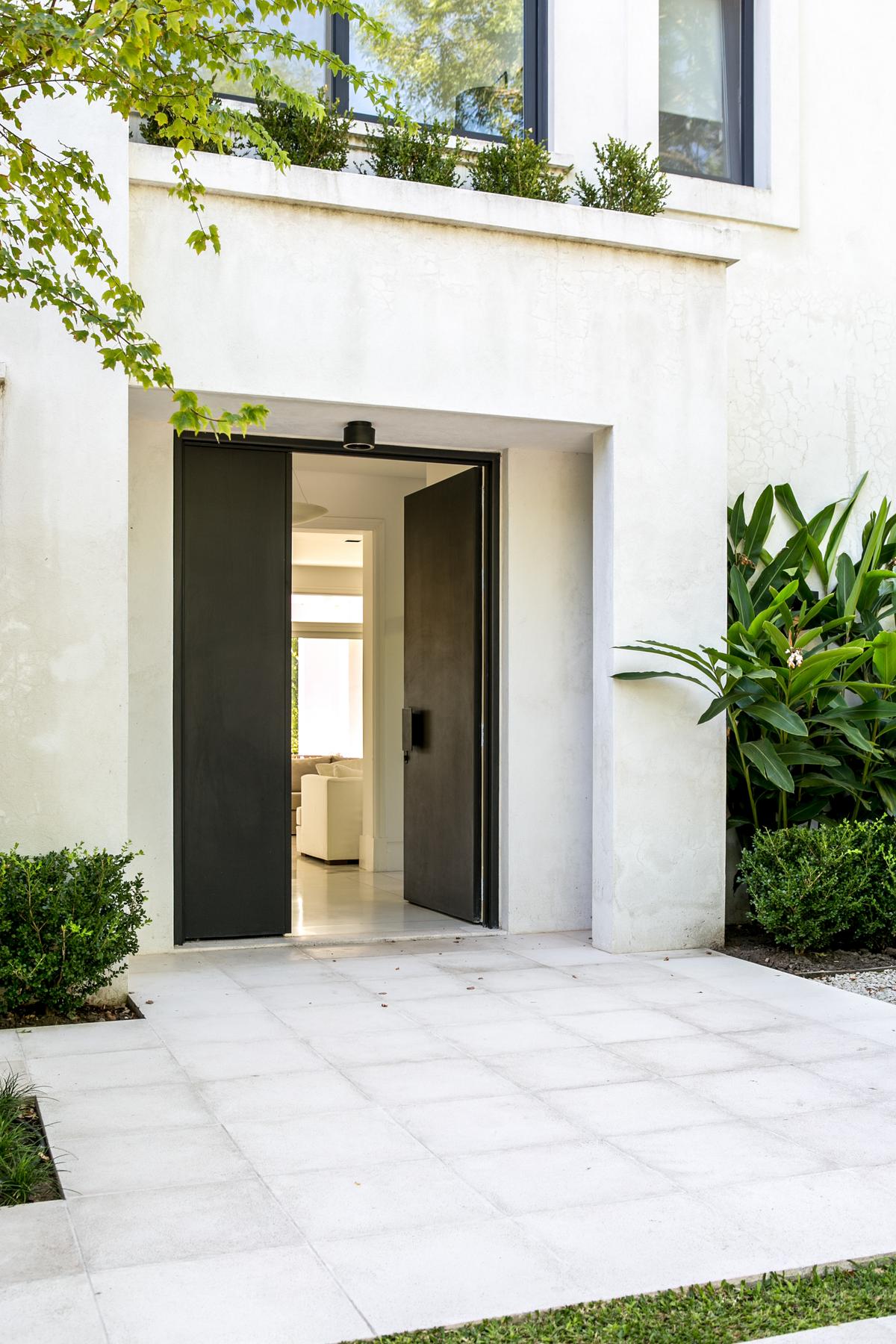 Fachada moderna com portas duplas pivotantes de metal preto e concreto branco — projeto Club Newman 3, por Escalante Vela Arquitectos, em Benavidez