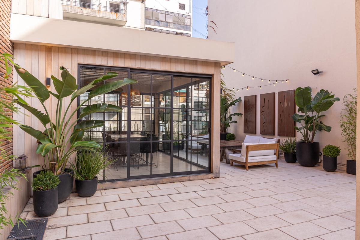 Pátio moderno semi-coberto com sofás brancos e vegetação — projeto Terraza en la ciudad, por Casa Cunia, em CABA