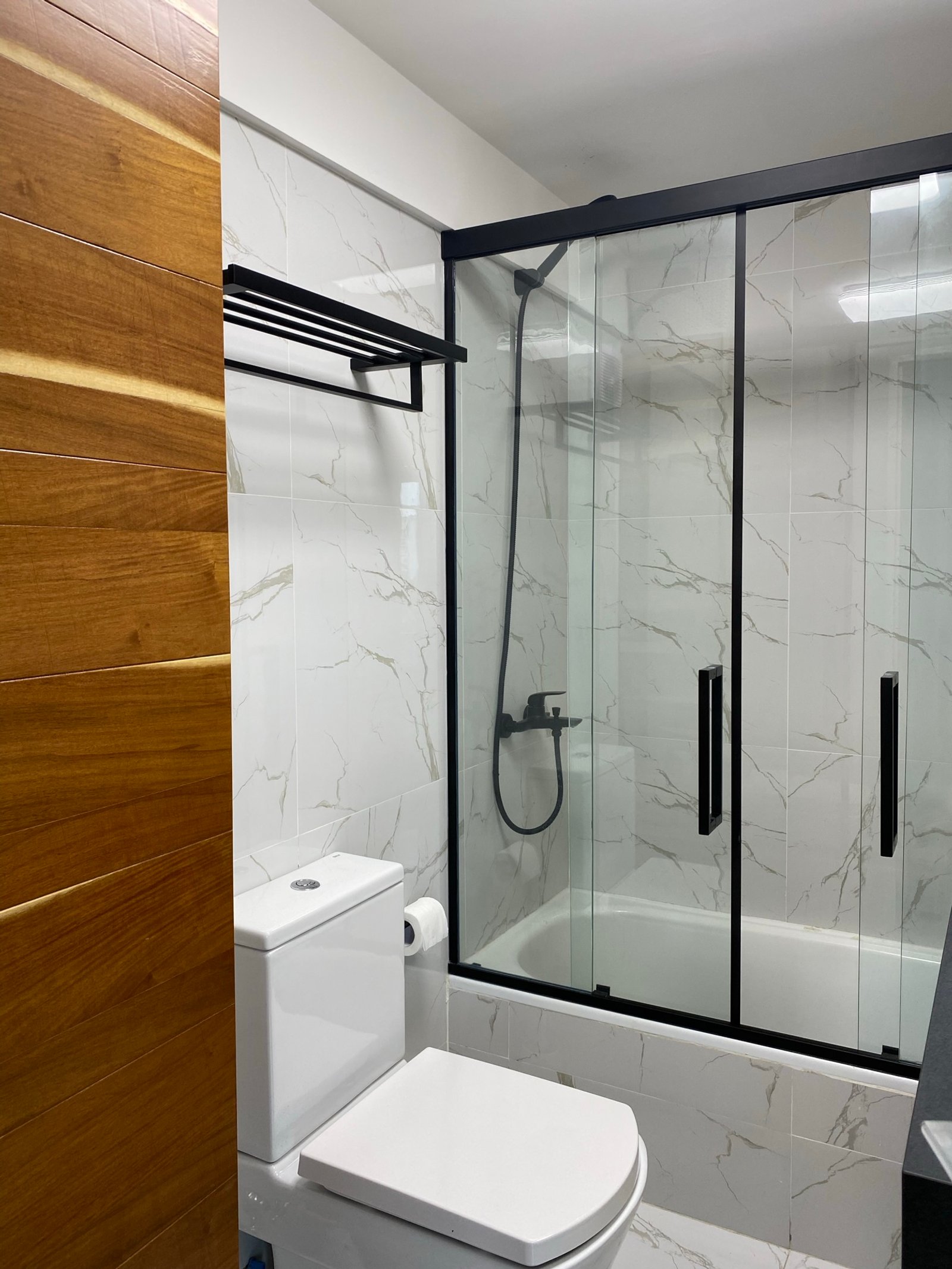Baño moderno con paredes de mármol, madera y detalles negros — proyecto Pringles, por MDBK Arquitectura, en Almagro