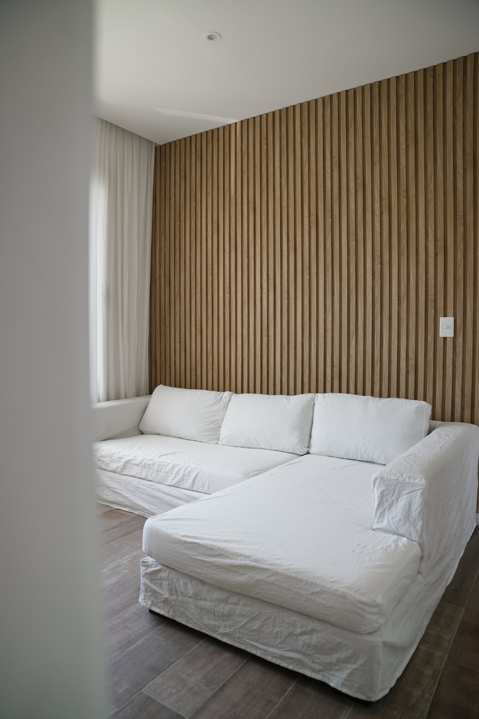 Living moderno con pared de listones de madera y sofá blanco — proyecto Play, por CASA1-TROMEN, en Bella Vista