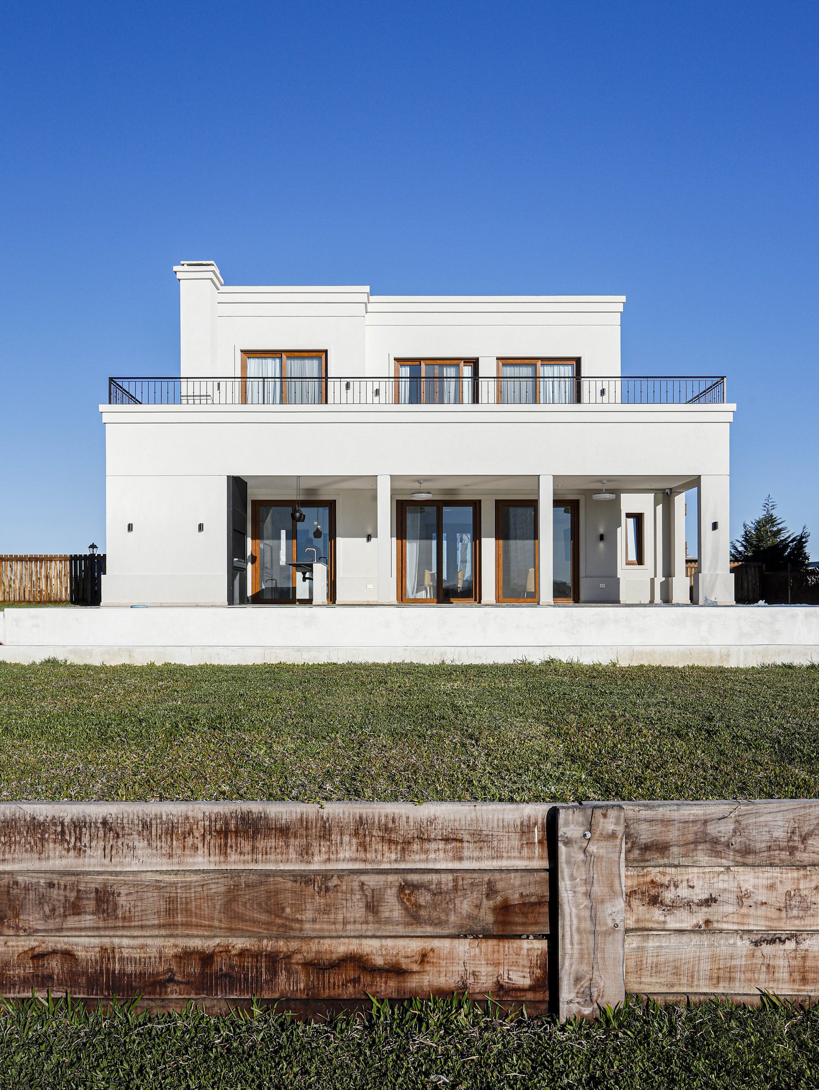 Fachada moderna blanca con césped y muro de madera — proyecto Casa SS182, por EZ architects, en M3CV+6H