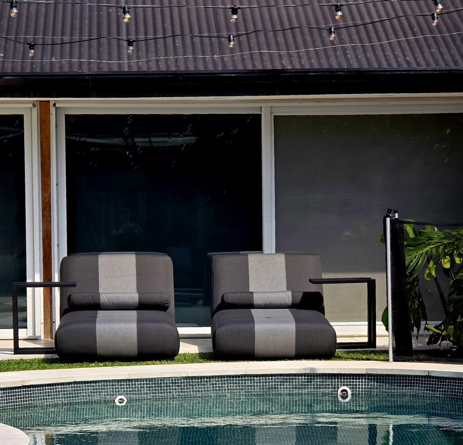 Poltronas listradas perto da piscina com luzes suspensas — projeto Reposeras de Aluminio, por Casa Nuñez
