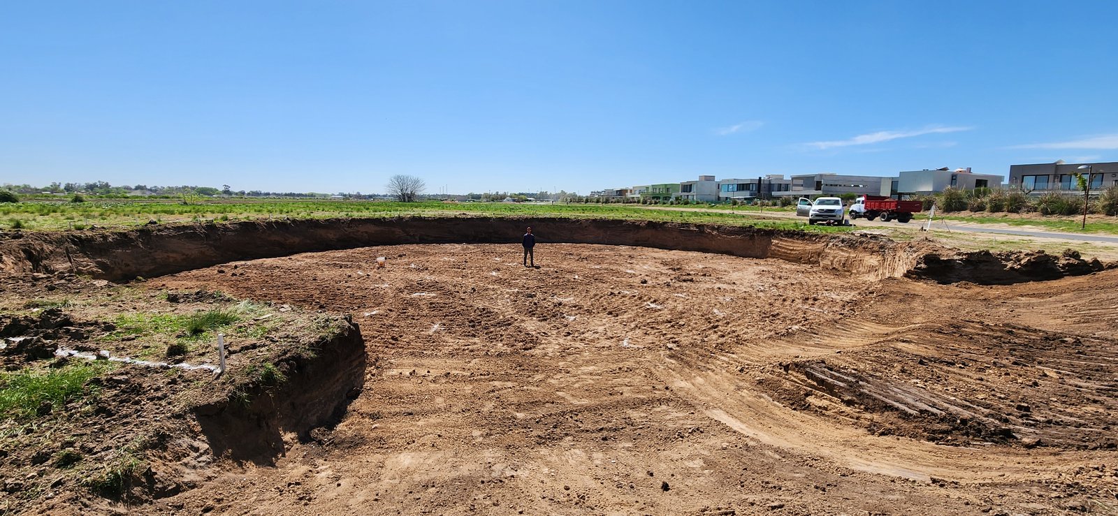 Gran excavación circular en terreno suburbano, bajo cielo azul — proyecto Central Park - Terralagos, por Estudio Rifahi, en Canning
