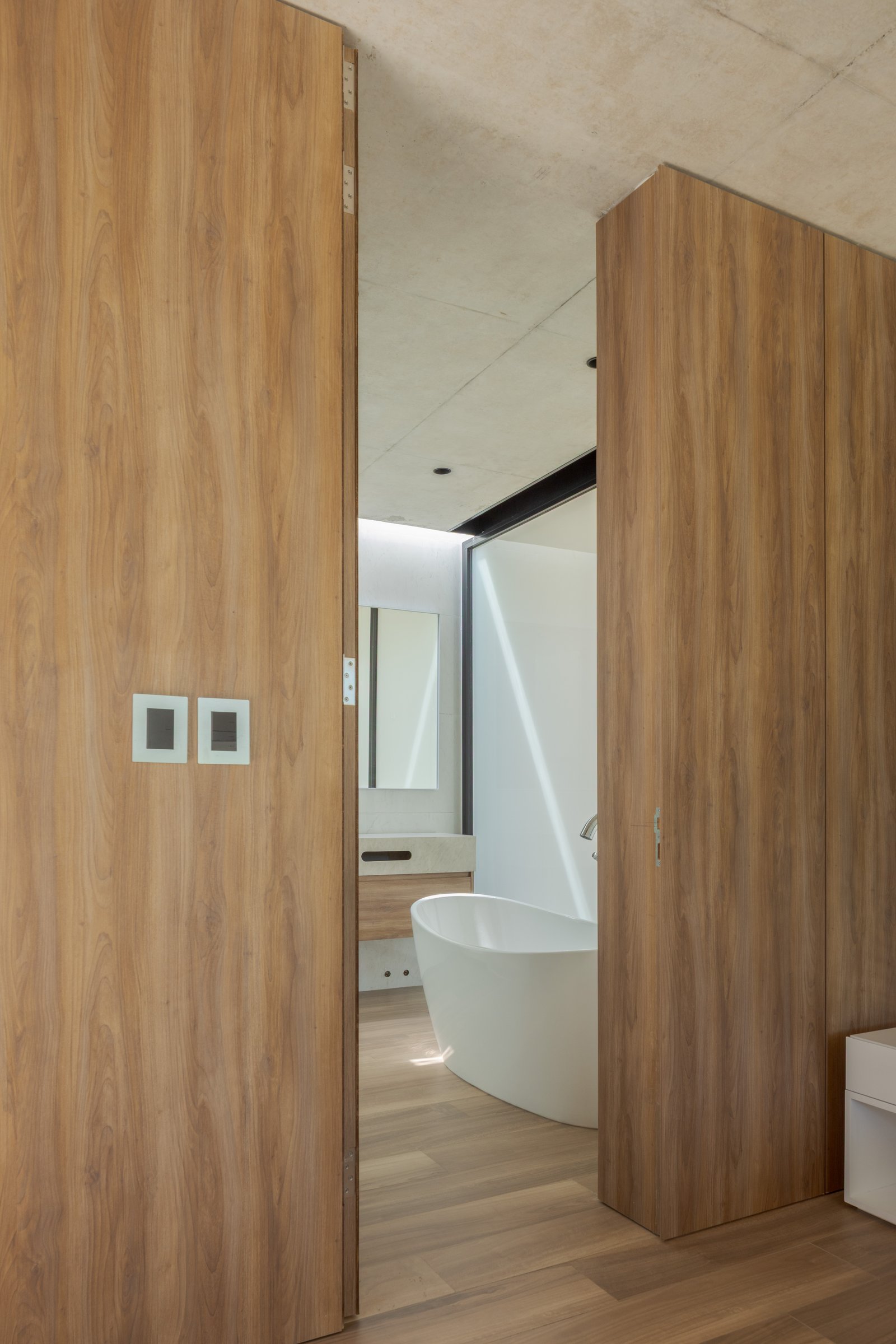Baño moderno con revestimiento de madera, bañera exenta y techo de hormigón — proyecto Casa PLANALTO, por Grupo CRBN, en Av. Pres. Perón 10298