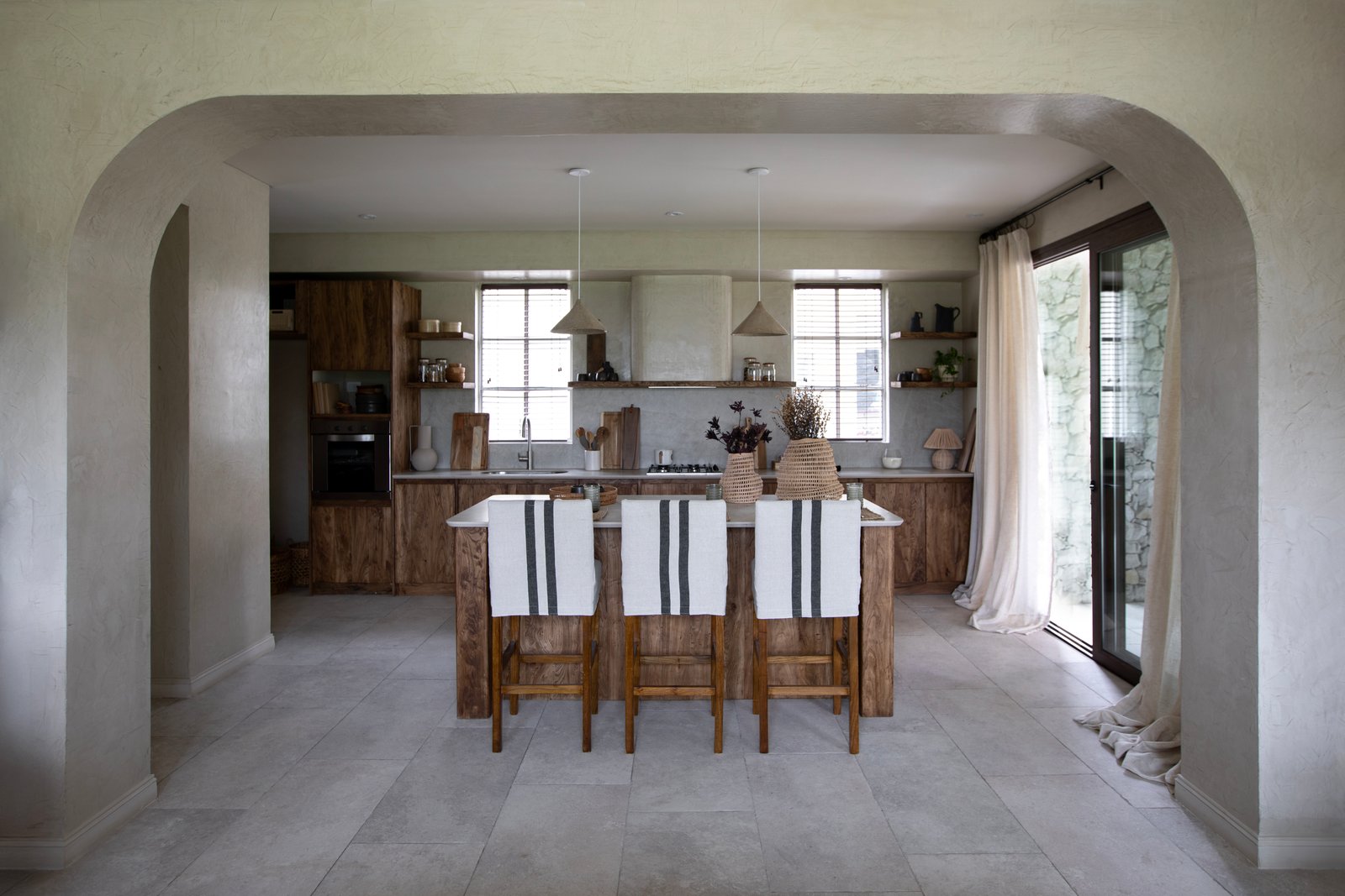 Cocina mediterránea abierta con isla, sillas a rayas y arcos — proyecto OBRA EL DESCANSO, por ILVA, en Provincia de Buenos Aires