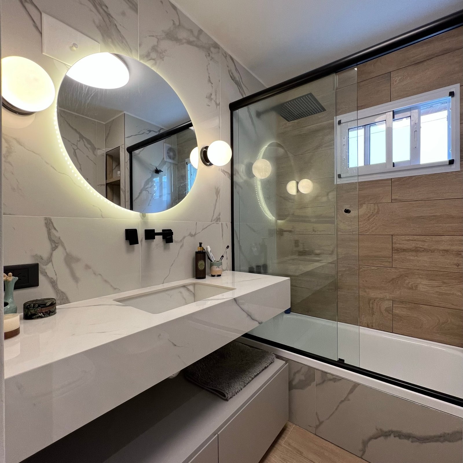 Baño moderno con espejo redondo retroiluminado y mármol — proyecto Diaz Velez I, por MDBK Arquitectura, en Almagro