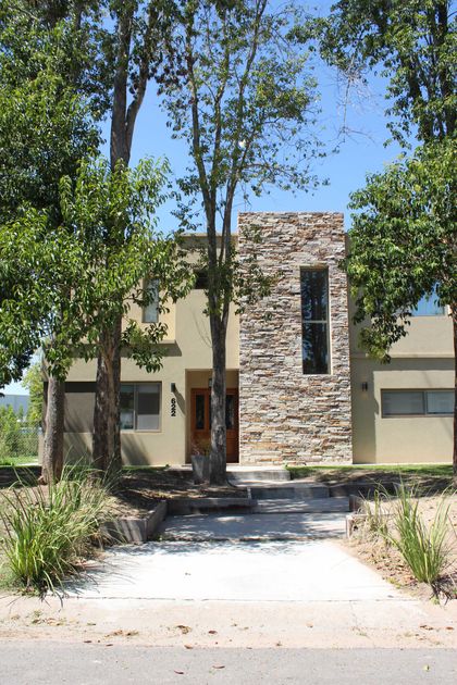 Fachada moderna con detalles en piedra y vegetación exuberante — proyecto San Matias, por CASTRO SANCHEZ ARQUITECTOS, en Belén de Escobar