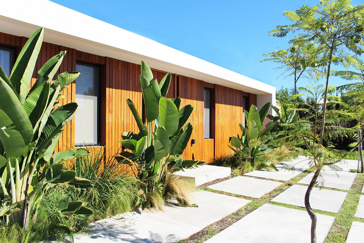Fachada moderna com madeira, vidro e vegetação exuberante — projeto Casa Las Liebres, por Mazzinghi Sanchez, em Garin