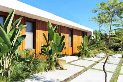 Fachada moderna con madera, vidrio y vegetación exuberante — proyecto Casa Las Liebres, por Mazzinghi Sanchez, en Garin