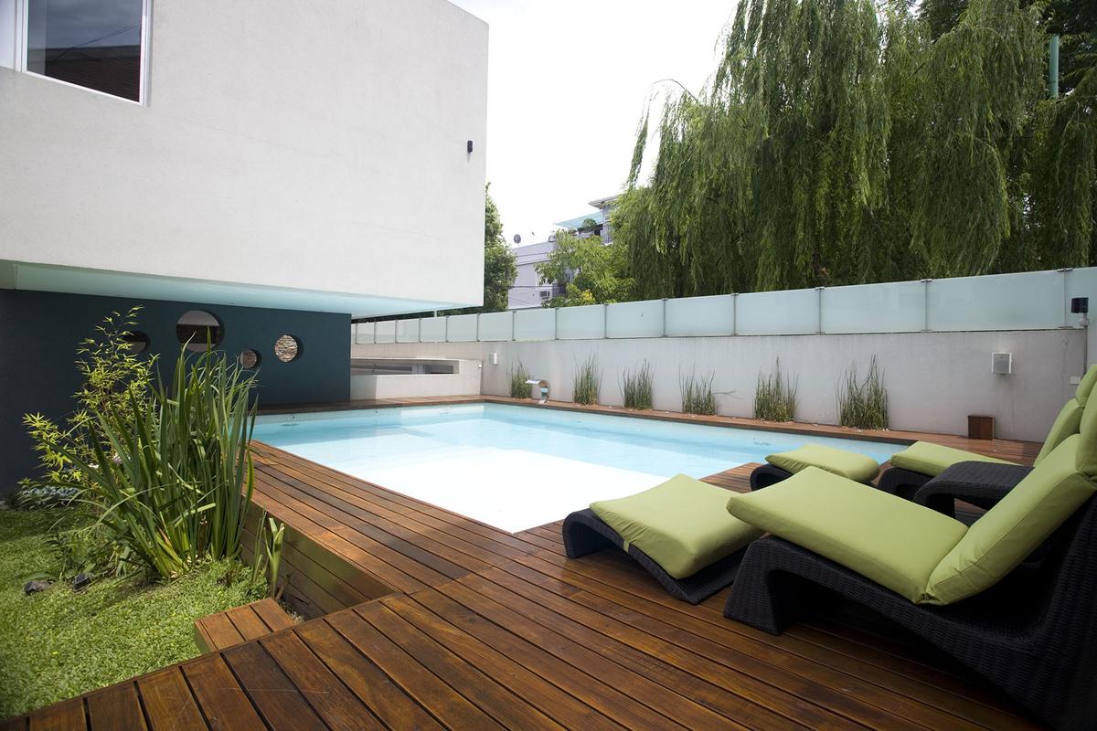 área de piscina moderna com deck de madeira e vegetação exuberante — projeto Devoto, por Remy Arquitectos, em CABA