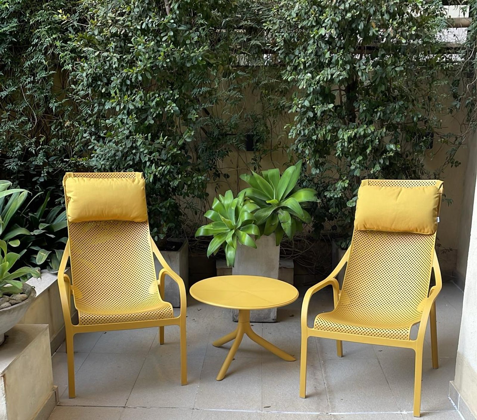 Duas cadeiras e mesa amarelas em pátio com vegetação exuberante — projeto Living Exterior, por Casa Nuñez