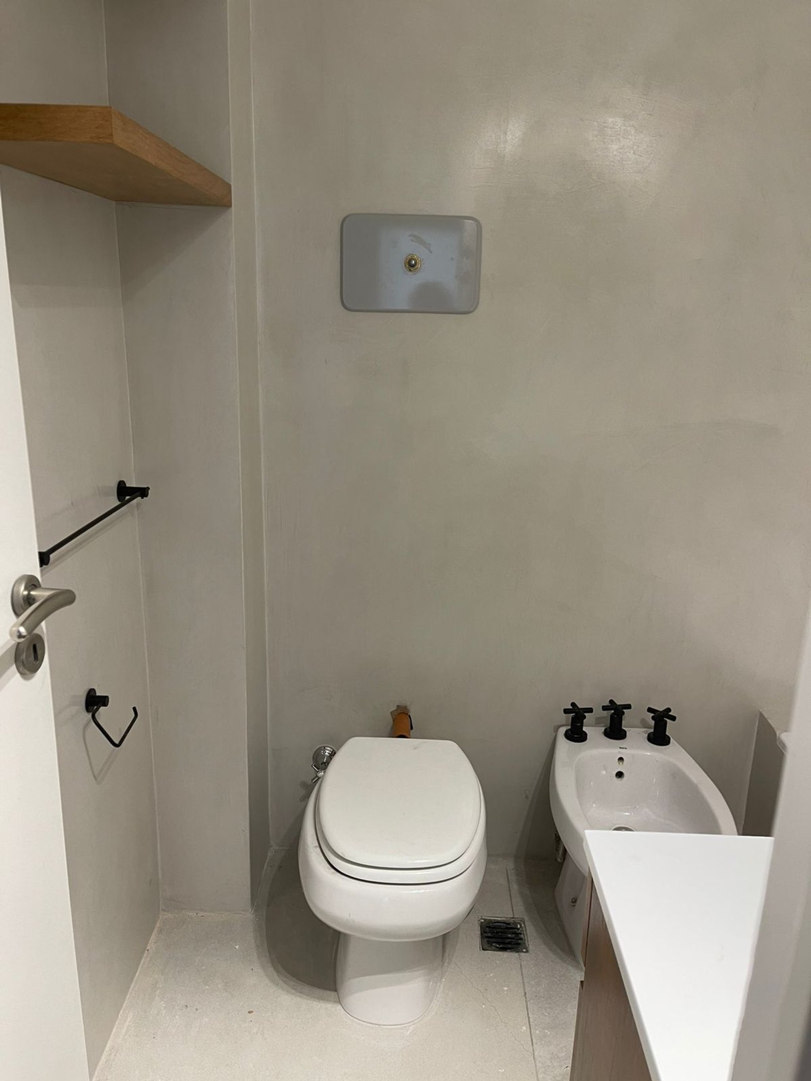 Baño moderno con bidet y inodoro, paredes de microcemento y estante de madera — proyecto Olazabal, por Estudio NET Arquitectura , en Olazábal 3228